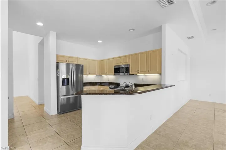Kitchen with kitchen peninsula, light brown cabinets, light tile patterned floors, and stainless steel appliances