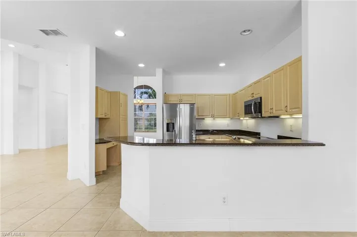 Kitchen featuring dark stone counters, stainless steel appliances, kitchen peninsula, and light tile patterned floors