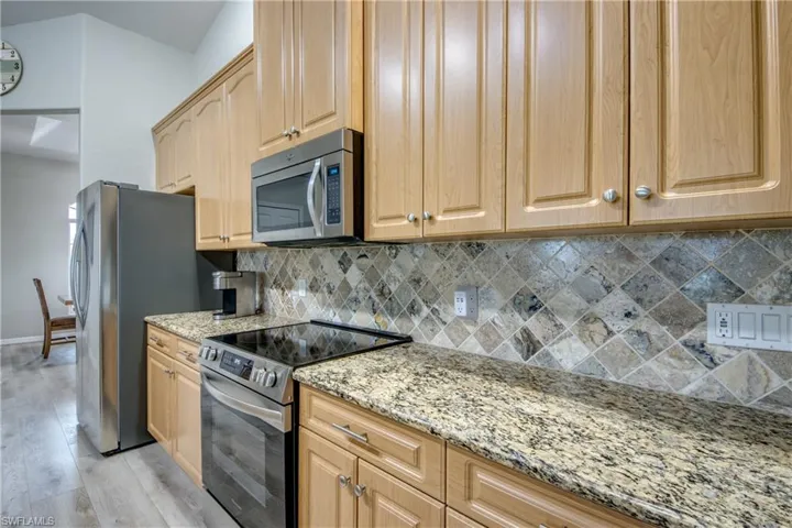 Kitchen featuring appliances with stainless steel finishes, light wood-style flooring, light stone counters, light brown cabinetry, and backsplash
