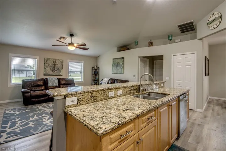 Kitchen featuring open floor plan, ceiling fan, light wood-style floors, light stone countertops, and vaulted ceiling
