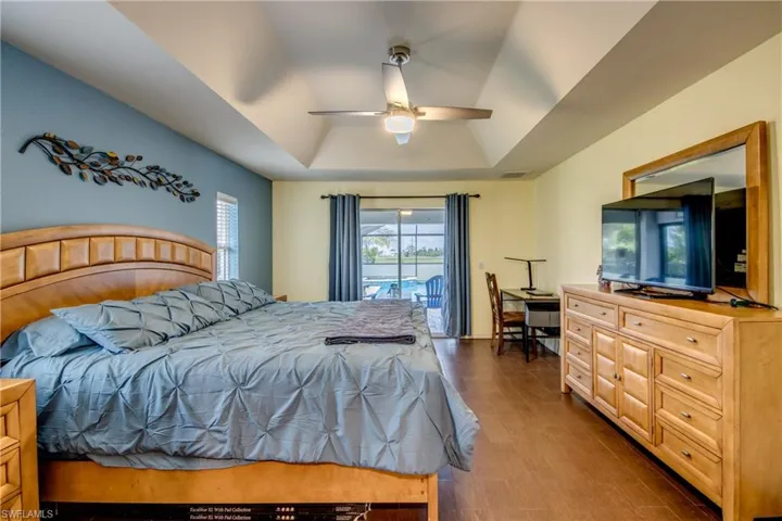 Bedroom with a raised ceiling, access to exterior, dark wood-style flooring, and a ceiling fan