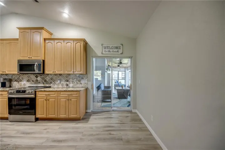 Kitchen with appliances with stainless steel finishes, lofted ceiling, backsplash, light stone countertops, and light wood finished floors