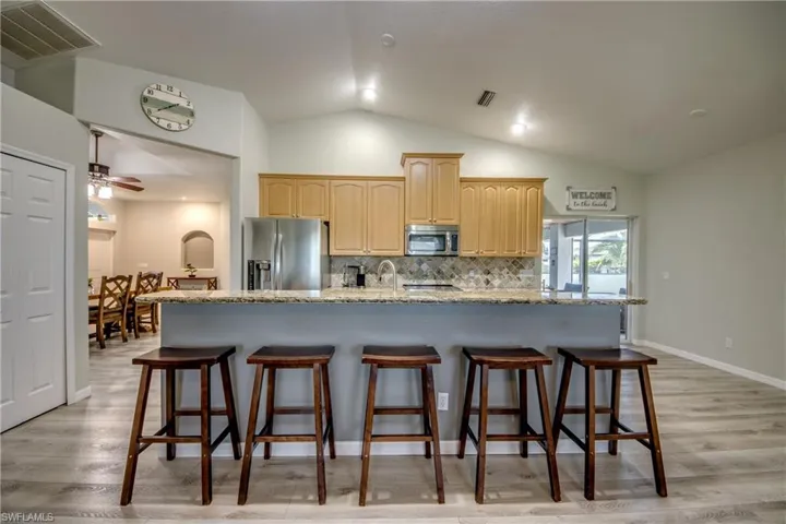Kitchen with appliances with stainless steel finishes, light brown cabinetry, lofted ceiling, a breakfast bar, and decorative backsplash