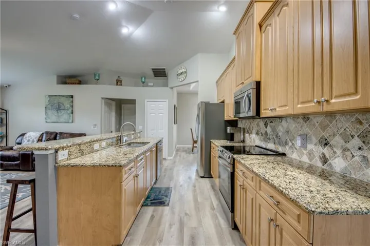 Kitchen with appliances with stainless steel finishes, vaulted ceiling, light wood finished floors, a center island with sink, and a kitchen bar