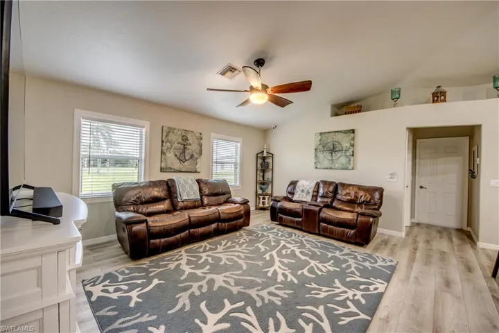 Living room featuring a ceiling fan, light wood-style floors, and lofted ceiling