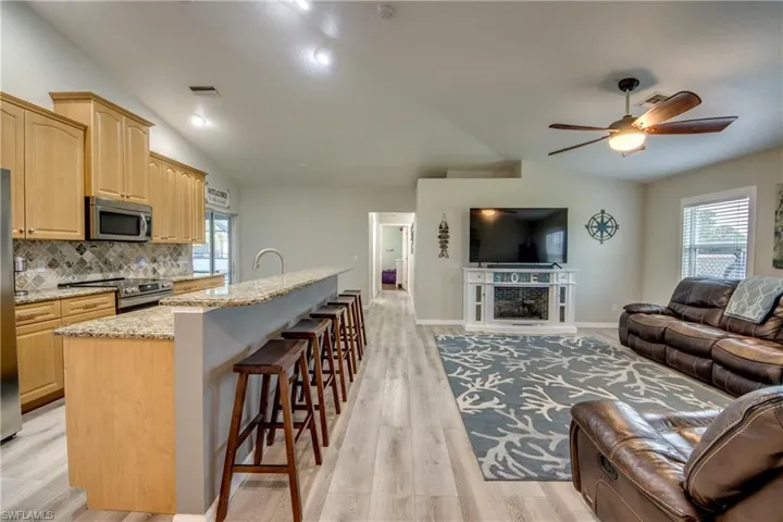 Living room with vaulted ceiling, light wood-style floors, ceiling fan, and healthy amount of natural light