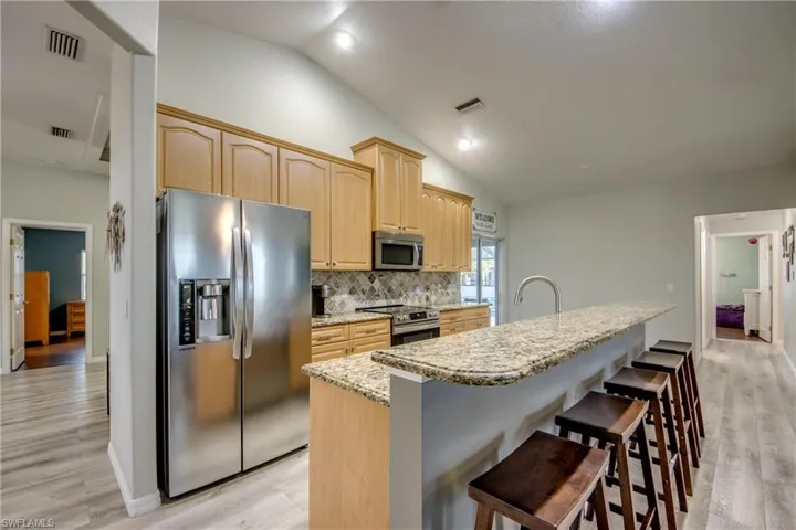 Kitchen with appliances with stainless steel finishes, vaulted ceiling, decorative backsplash, light brown cabinets, and light wood-style floors