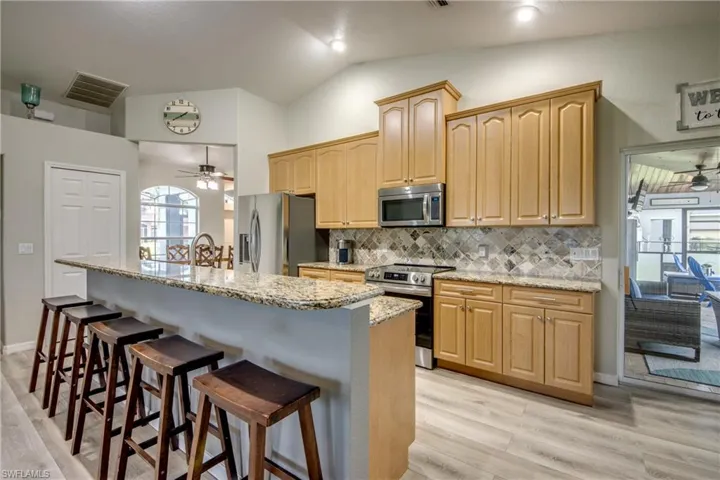 Kitchen with appliances with stainless steel finishes, ceiling fan, a breakfast bar, light wood-type flooring, and vaulted ceiling