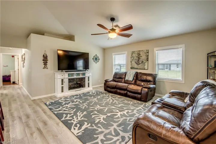 Living area featuring ceiling fan, wood finished floors, lofted ceiling, and a fireplace with raised hearth