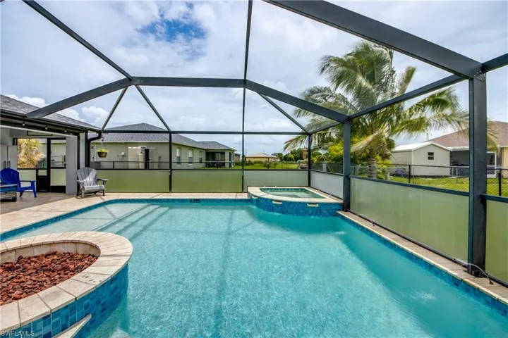 View of swimming pool featuring a pool with connected hot tub, glass enclosure, an outdoor fire pit, and a patio