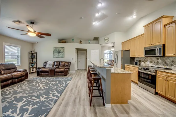 Kitchen featuring appliances with stainless steel finishes, ceiling fan, open floor plan, light stone countertops, and lofted ceiling