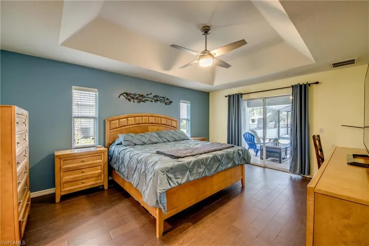 Bedroom with a tray ceiling, access to exterior, dark wood-style flooring, and ceiling fan