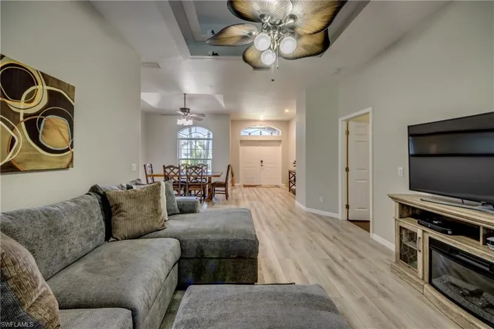 Living room with a ceiling fan, light wood-type flooring, and a tray ceiling