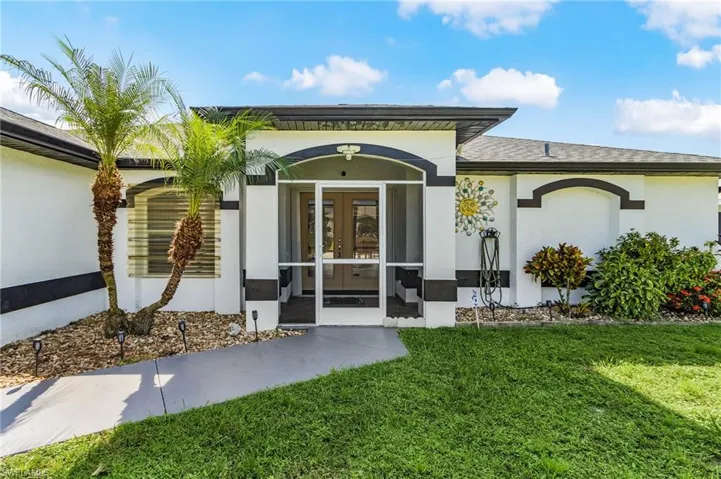Doorway to property with stucco siding, a lawn, french doors, and a sunroom