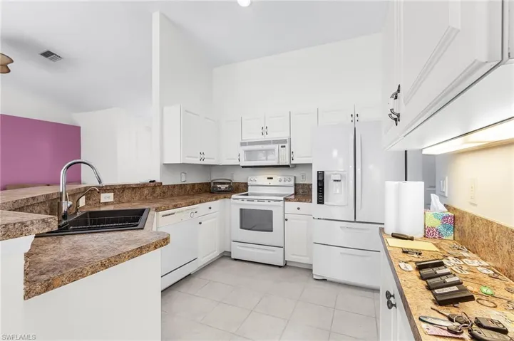 Kitchen with white appliances, white cabinetry, light tile patterned flooring, and a peninsula