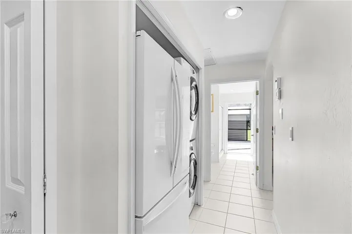 Laundry room featuring light tile patterned floors, recessed lighting, and stacked washing machine and dryer