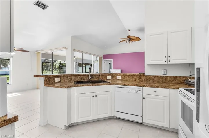 Kitchen with ceiling fan, dark countertops, white appliances, white cabinets, and lofted ceiling