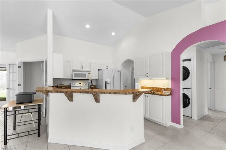 Kitchen with dark countertops, a kitchen bar, arched walkways, white cabinets, and high vaulted ceiling
