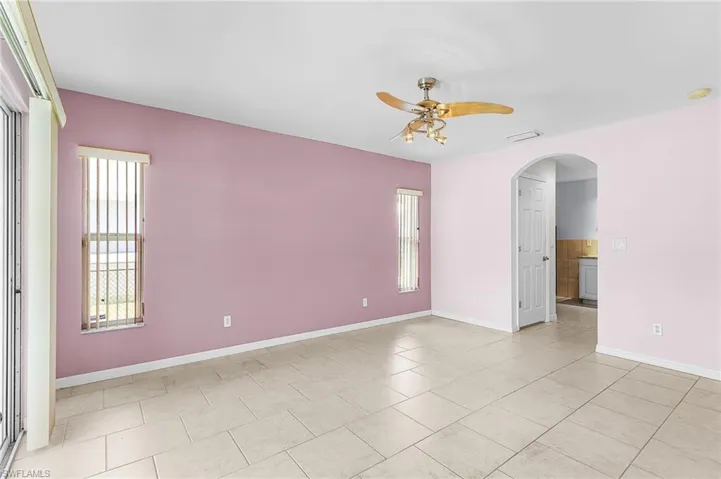 Empty room featuring ceiling fan, arched walkways, and light tile patterned flooring
