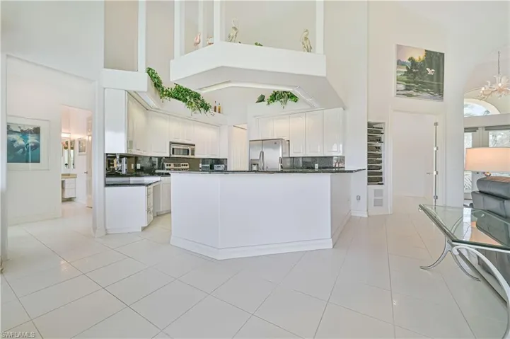 Kitchen with a high ceiling, granite counters, white cabinets, backsplash, and appliances with stainless steel finishes