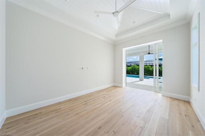 The primary bedroom features a vaulted ceiling with nickel gap treatment and ample natural light through the windows and sliding glass doors leading out the pool and spa.