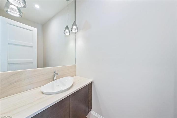 The powder bath is tucked away just off of the kitchen. The floating slab door vanity, wall-to-wall mirror, and ceiling pendants give this room a sleek and contemporary feel.