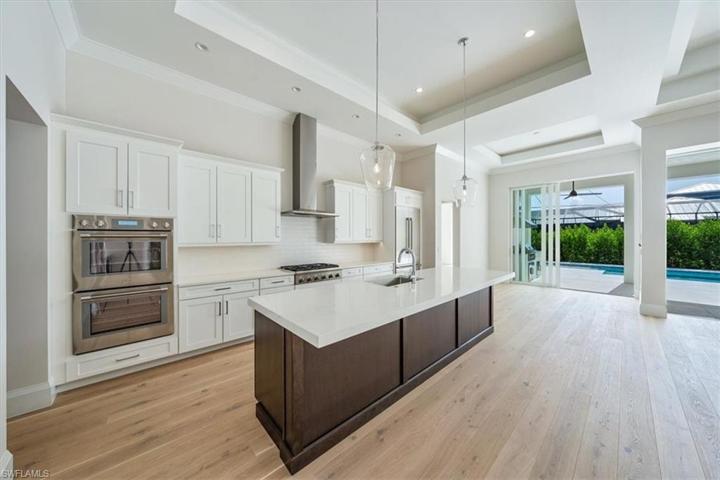 The kitchen overlooks the great room, open dining, and pocket sliders leading out to the pool deck with outdoor kitchen.