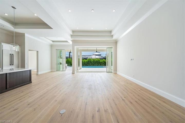 Lot 13 features the Dune plan, with an open concept main living area with soaring 12' tray ceilings, wide plank wood flooring, and pocket impact glass sliding glass doors leading out to the pool deck.