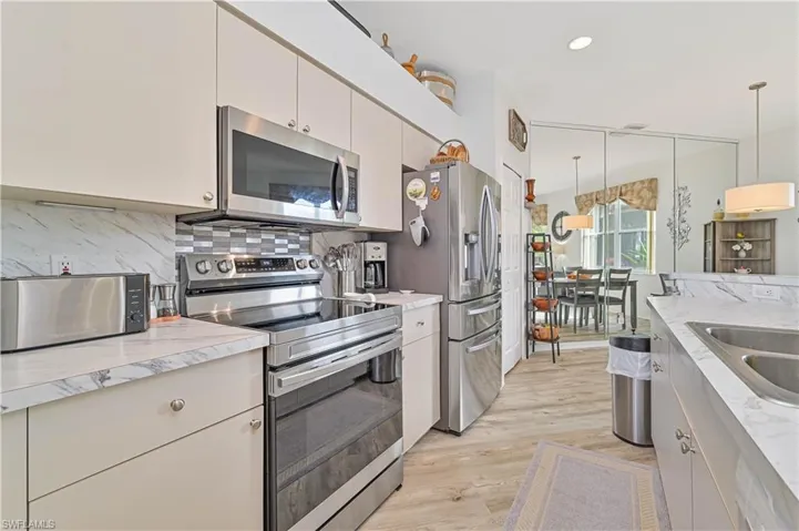 Kitchen featuring stainless steel appliances, sink, backsplash, hanging light fixtures, and light wood-type flooring