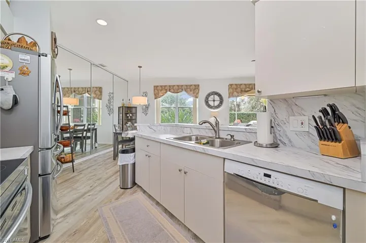 Kitchen with white cabinetry, stainless steel appliances, decorative backsplash, decorative light fixtures, and sink