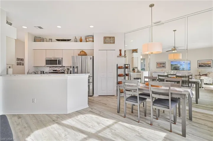 Kitchen with light hardwood / wood-style floors, decorative backsplash, hanging light fixtures, appliances with stainless steel finishes, and white cabinets