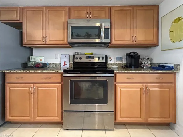Kitchen with stainless steel appliances, dark stone countertops, light tile patterned floors, and brown cabinets