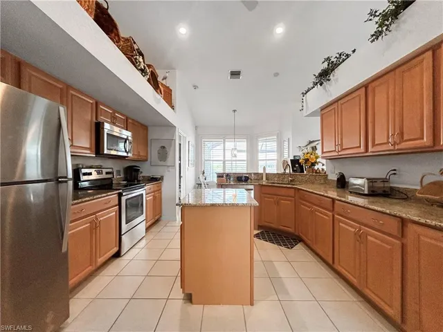 Kitchen featuring dark stone counters, stainless steel appliances, brown cabinets, a peninsula, and recessed lighting