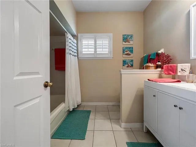 Bathroom featuring shower / bathtub combination with curtain, vanity, and light tile patterned floors