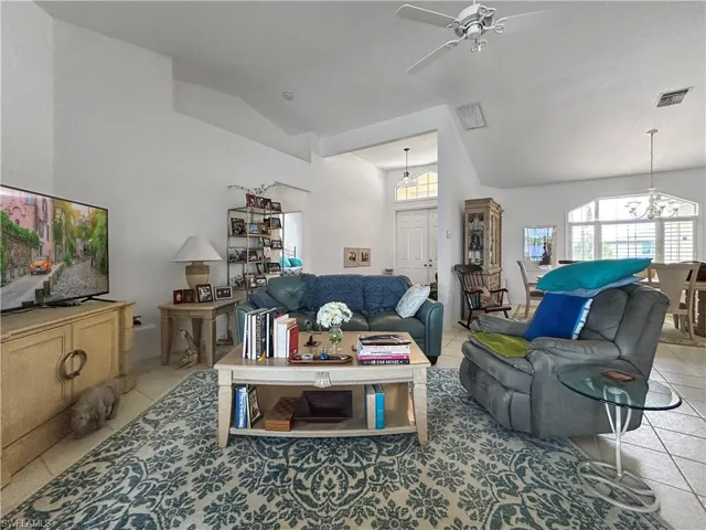 Living room with light tile patterned floors, vaulted ceiling, a chandelier, and a ceiling fan