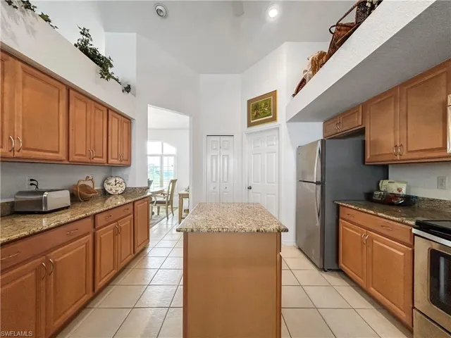 Kitchen featuring brown cabinets, light stone countertops, stainless steel appliances, a center island, and light tile patterned flooring