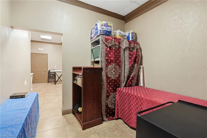Bedroom with a textured wall, light tile patterned floors, and crown molding