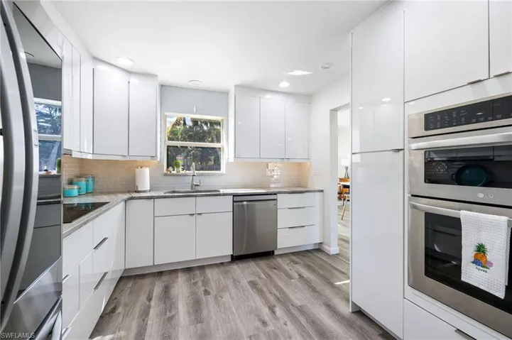 Kitchen featuring decorative backsplash, stainless steel appliances, sink, light hardwood / wood-style flooring, and white cabinets