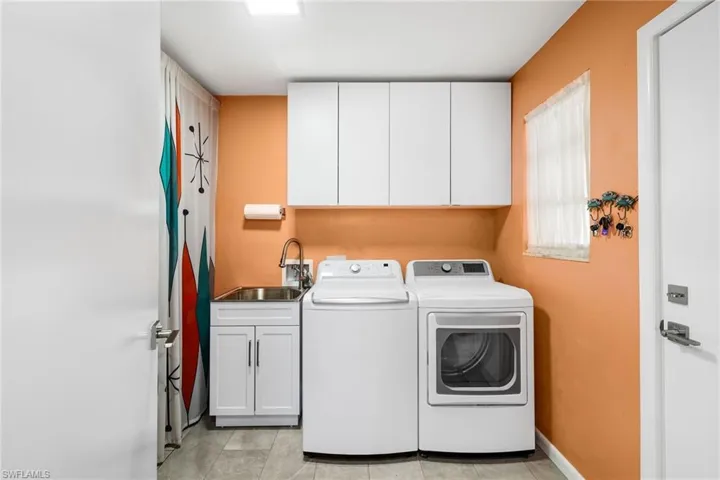 Clothes washing area with cabinets, independent washer and dryer, sink, and light tile patterned floors