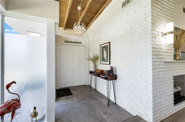 Foyer entrance with wooden ceiling, dark tile patterned flooring, beamed ceiling, a notable chandelier, and brick wall