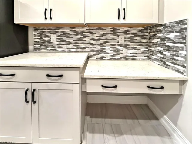 Kitchen view of white cabinetry, backsplash, and light stone countertops