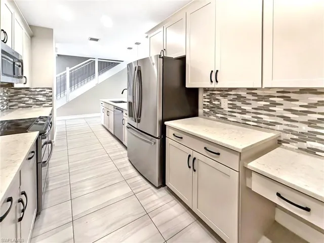 Kitchen featuring decorative backsplash, appliances with stainless steel finishes, light stone counters, light tile patterned flooring, and white cabinets