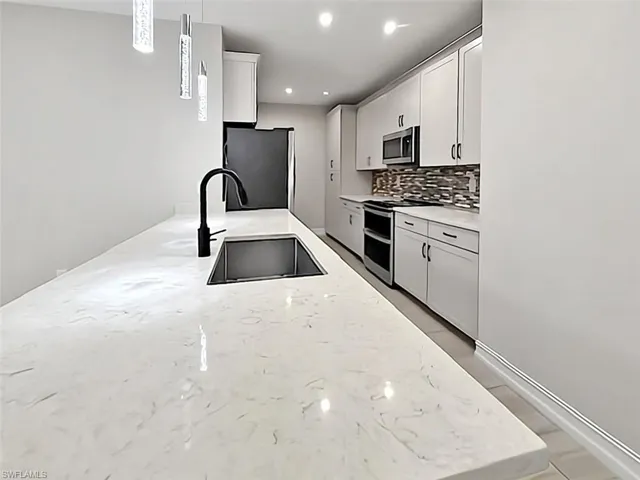 Kitchen with appliances with stainless steel finishes, light stone countertops, white cabinets, decorative backsplash, and pendant lighting