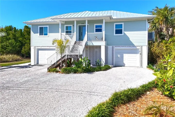 Coastal inspired home with an attached garage, a standing seam roof, gravel driveway, and covered porch