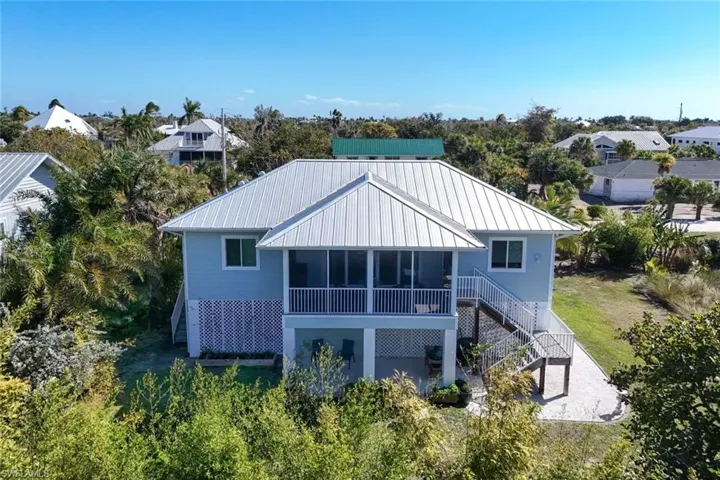 Back of property featuring a patio, a standing seam roof, a residential view, a sunroom, and view of wooded area
