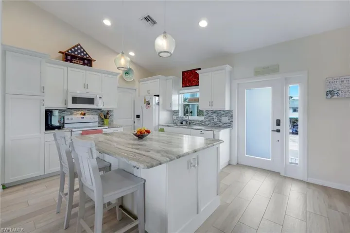 Kitchen with vaulted ceiling, white cabinets, decorative light fixtures, a breakfast bar area, and white appliances