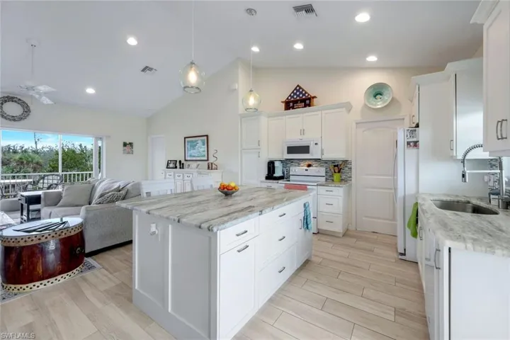 Kitchen featuring hanging light fixtures, white cabinetry, white appliances, wood tiled floors, and light stone countertops