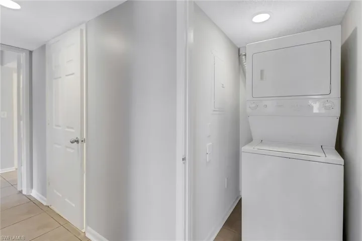 Clothes washing area with light tile patterned flooring and stacked washing maching and dryer