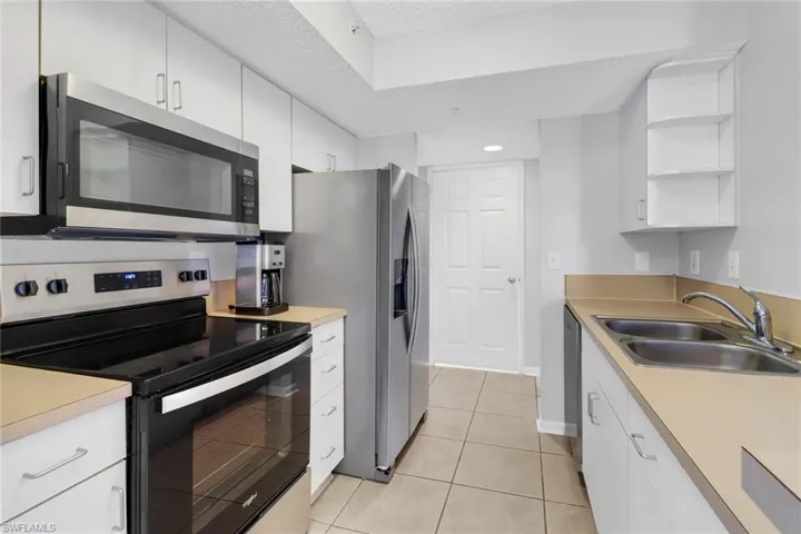 Kitchen with appliances with stainless steel finishes, a textured ceiling, sink, light tile patterned floors, and white cabinetry