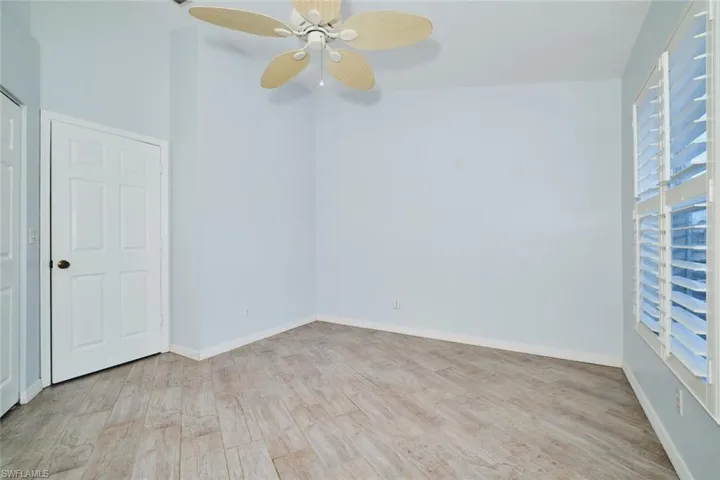 Guest bedroom with lofted ceiling, light wood-like tile floors, plantation shutters and ceiling fan